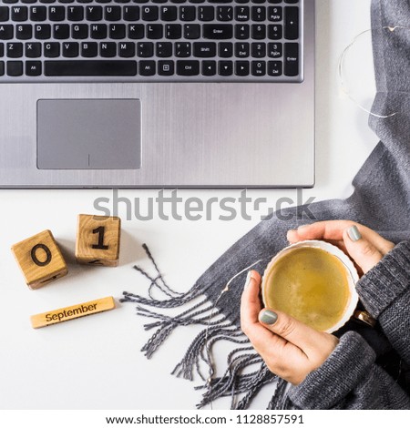 September 1 date on the wooden calendar. At the autumn workplace behind the computer, next to the scarf and a cup of coffee in woman's hands. Top view, flat lay