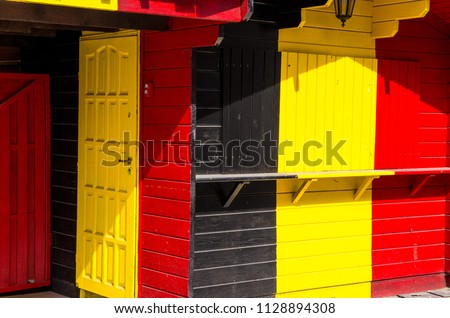Wooden building with combination of Belgium Belgien and Germany Deutschland flag colors: black, red, yellow with doors and lamp lantern