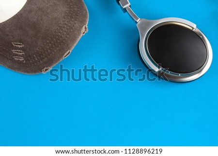 Baseball cap in the left corner and headphones in the right corner on a blue background top view