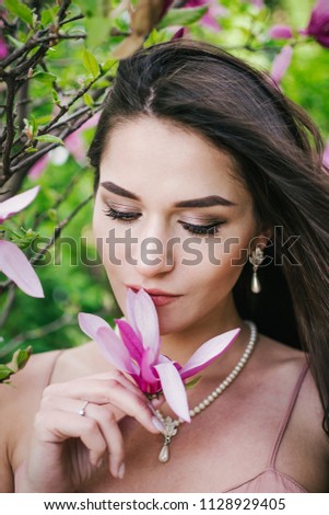 Portrait of young beautiful woman with long curly hair between pink magnolia tree, close up
