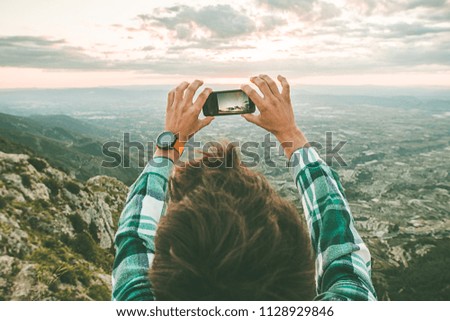 Man taking a photo with his mobile phone to a sunset. Guy taking a picture of a sunset in the mountains.