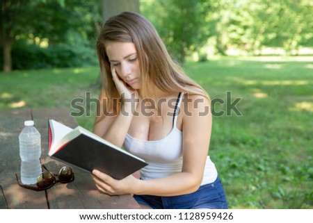 Teenage girl reading a book in the park sitting at a bench