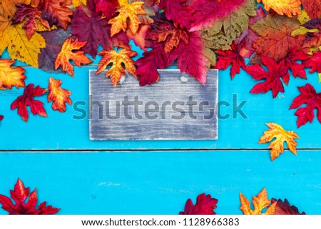 Blank wood sign with colorful fall leaves border and antique rustic teal blue wooden background; autumn, Thanksgiving, Halloween, seasonal nature background with copy space