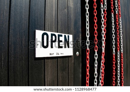 White Open Sign Attached To Brown Wooden Wall Next To Museum Entrance With Hanging Beads