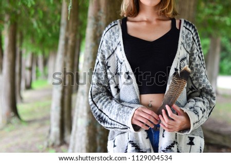 young woman in forest holding feather in boho cardigan