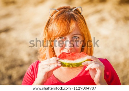 Beautiful Caucasian girl with funny ears eating watermelon with enjoyment. Summer vacation fun stock image. Happiness, weekend picnic.  