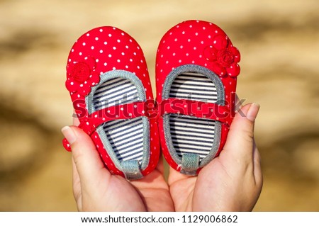 Young pregnant woman about to become mother holding tiny red baby girl shoes. Expecting a girl daughter concept image. Expecting mother, future parent.