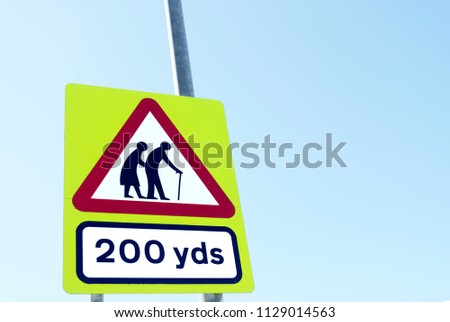 Elderly senior old citizens crossing road safety sign blue sky background