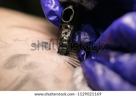 A professional tattoo artist introduces ink into the skin using a needles from a tattoo machine. tattoo art on body.Makes a tattoo.Professional tattooist working tattooing in studio.Selective focus