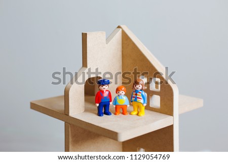 Three toy figures of men-a man, a woman and a child in a wooden toy house. A symbol of a family in their own new home. Close up.
