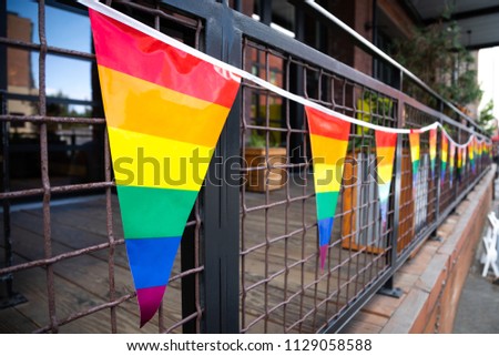 Wide angle close up on strand of rainbow LGBTQ pride flags on an outdoor patio railing, with space for text on right
