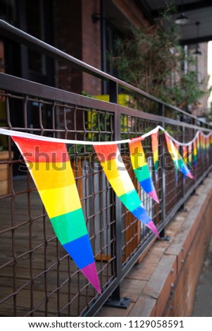 Row of rainbow LGBTQ pride flags on an outdoor patio railing, with space for text on top