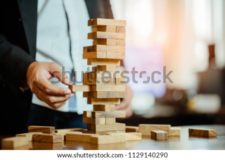 business man hand  pulling out or placing wood block on the tower in modern office. plan and strategy in business. blur for background.