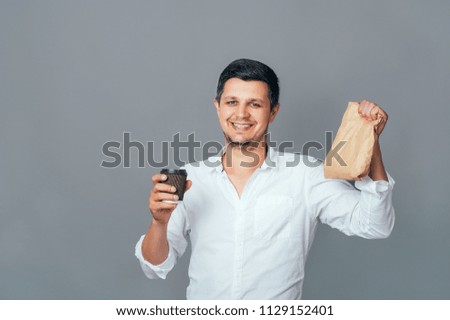 Handsome young businessman holding brown paper packet with take away food and cup of coffee. Business lunch fast food students Lifestyle Dinner Street food People