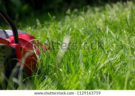 A close up image of a lawnmower on a lawn of long grass in need of cutting