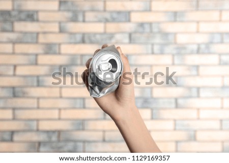 Woman holding crumpled aluminum can on brick wall background. Metal waste recycling