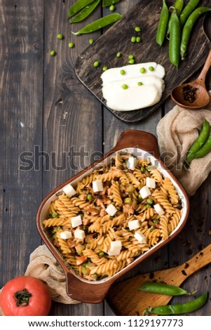 Fusilli pasta with zucchini, goat cheese and green peas on a dark rustic background