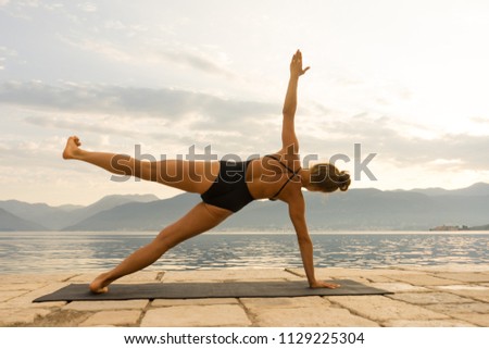 young healthy Woman Doing Yoga at the Sea and Mountains. Silhouette during sunrise with natural sunlight outdoor.