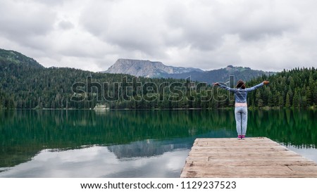 The girl stands with her hands up on the pier of black lake in the national Park Durmitor. Montenegro.