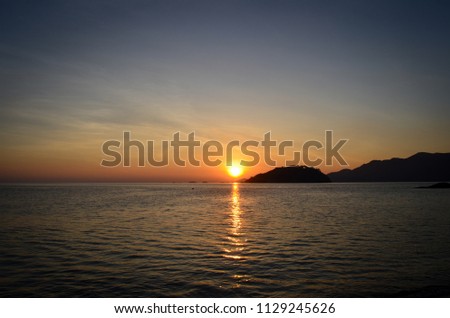 Silhouette photo of seascape in Thailand with beautiful color of sunset sky, mountains and reflection of the sun on sea water.