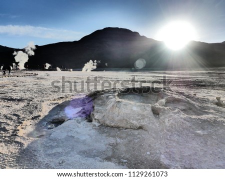 Visiting el Tatio, a geyser field located within the Andes Mountains of northern Chile near San Pedro de Atacama. The sun rises behind the mountains and blue sky and geysers eject hot water and steam.