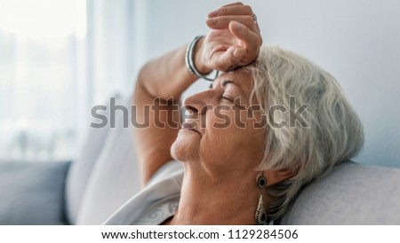 Thoughtful senior woman relaxing on bed. Senior woman relaxing at home. Woman having a nap on the sofa relaxing with her head tilted back on the cushion and eyes closed