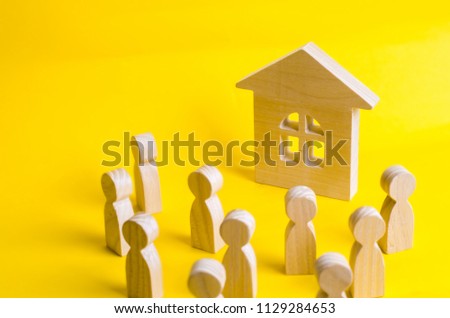 A group of wooden figures of people surround and look at the wooden house. Young people in search of affordable housing. Loans and loans for the purchase of a new home. Rent.