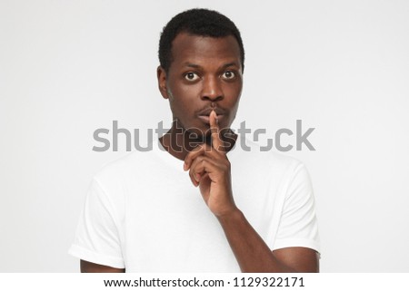 Young handsome African american man isolated on gray background wearing blank white t shirt and pressing index finger to lips as if asking other to keep silent about exciting secret