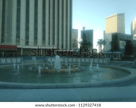 Spanish Plaza in New Orleans, Luisiana, United States of America. The picture was taken at sunset.  A Christmas tree is placed behind the fountain next to palm trees and in front of a large building. 