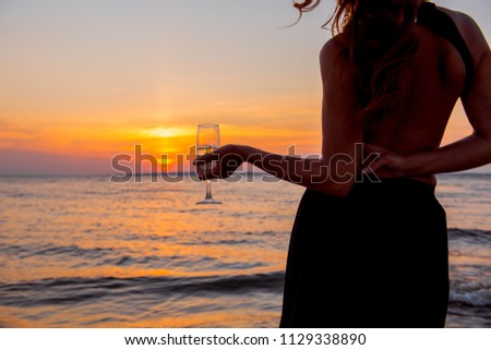 woman at sunset. Elegant girl is drinking champagne at sunset. Girl with  glass on background setting sun. romantic date in the evening. Luxury woman drinking from a wine glass on the beach. 
