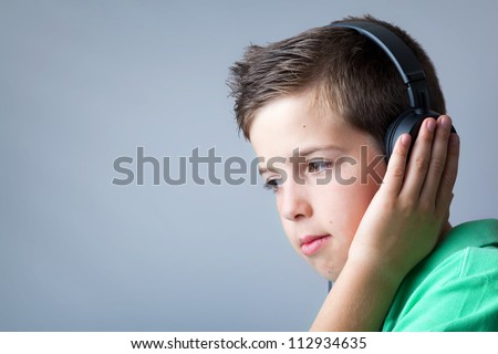 Portrait of a cute boy listening to music on headphones over grey background.