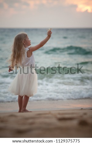 Adorable little girl with long hair looking at the sea. Rough sea. Flower in her arm.