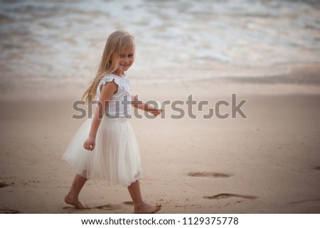 Adorable little girl with long hair walking on the beach. Rough sea. Flower in her arm.