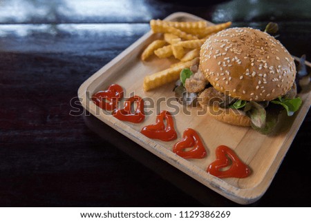Hamburger with french fries in wooden plate on dark wooden table