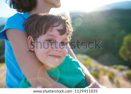 Portrait of a boy. Mom hugs her son. A woman spends time with a child in nature. A cute kid is sitting on my mother's hands.