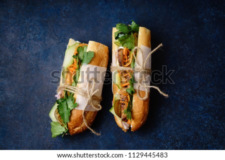 Classical banh-mi sandwich with sliced grilled pork tenderloin, shredded carrots and peeled cucumbers, jalapeno peppers and cilantro on dark blue background Royalty-Free Stock Photo #1129445483