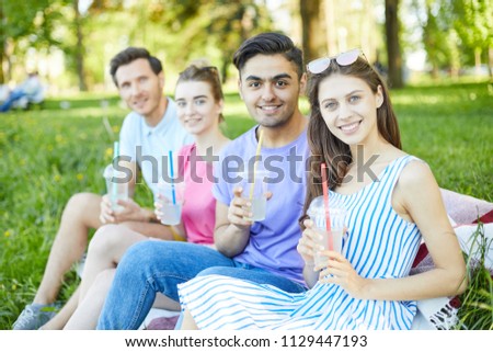 Two young couples with drinks looking at you during rest in natural environment