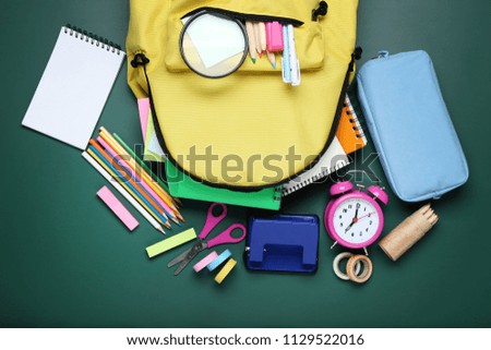 Yellow backpack with school supplies on green background