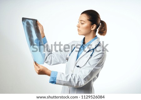 a young woman in a white coat and with a stethoscope on her shoulders holds an x-ray                             