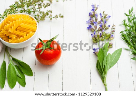 traditional mediterranean spices and vegetables with uncooked pasta on white wooden table background