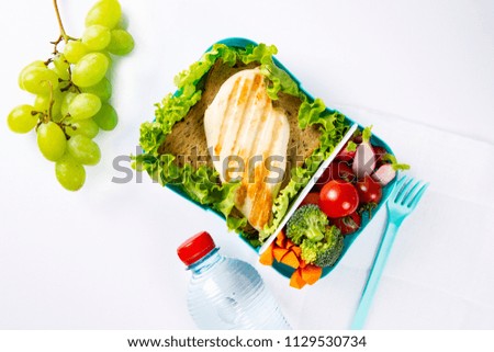 Plastic box with lunch and a bottle of water. Grilled chicken, bread and vegetables. The concept of healthy eating. Lunch for children. Business lunch. Top view. Copy space. The background is white.