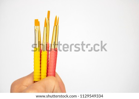 A hand holds bright pink and yellow paintbrushes on an isolated white background 