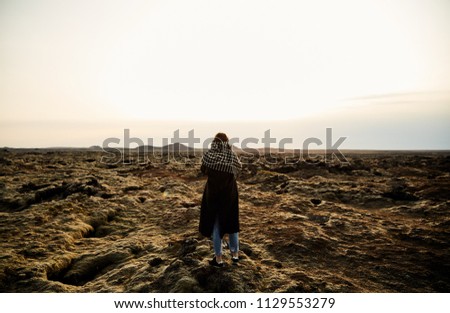 A young girl stands with her back and takes pictures of the landscape. The lava fields in Iceland. Post-apocalyptic landscape.