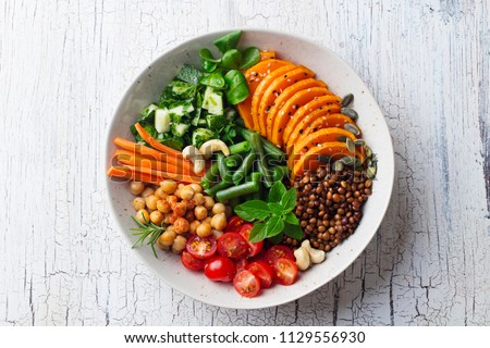 Healthy vegetarian salad. Lentil, chickpea, carrot, pumpkin, tomatoes, cucumber. Wooden background. Top view. Royalty-Free Stock Photo #1129556930
