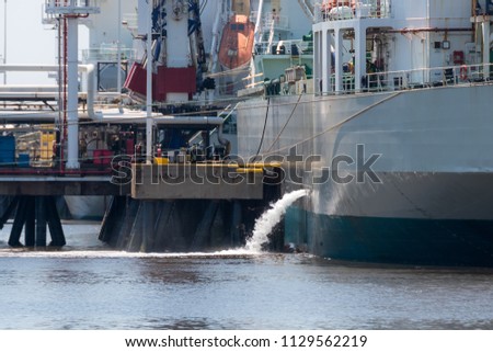 A tanker discharging ballast. The ship is docked at a pier. Lots of piping and machinery on the dock. Royalty-Free Stock Photo #1129562219
