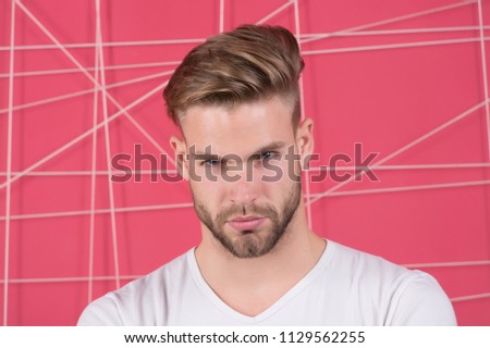 Man with bristle on strict concentrated face, pink background. Guy bearded and attractive with hairstyle. Masculinity concept. Man with beard or unshaven guy looks handsome and well groomed.
