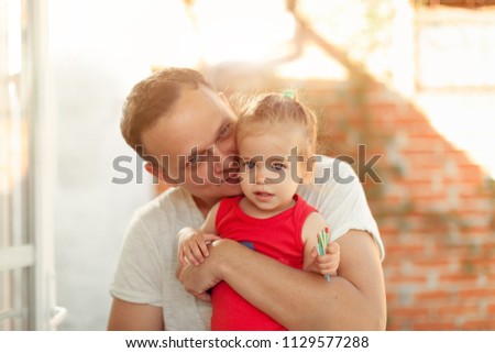 A young dad kisses his little daughter on the cheek and hugs her on the backyard in the summer Fathers day concept