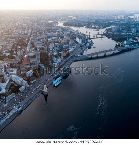 Panoramic view of a modern city with a river, unfinished bridge and park part of the city. Skyline bird eye aerial view with industrial zone and high-rise residential area under dramatic cloud sunset