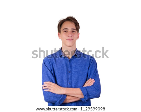 Young man looking at camera, smiling. Portrait of teen boy in blue jeans shirt, keeping arms crossed, isolated on white background