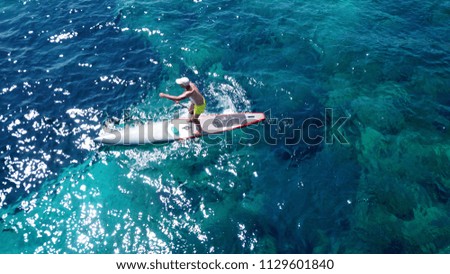 Aerial photo of fit man exercising SUP or Stand Up Paddle board in turquoise clear mediterranean island